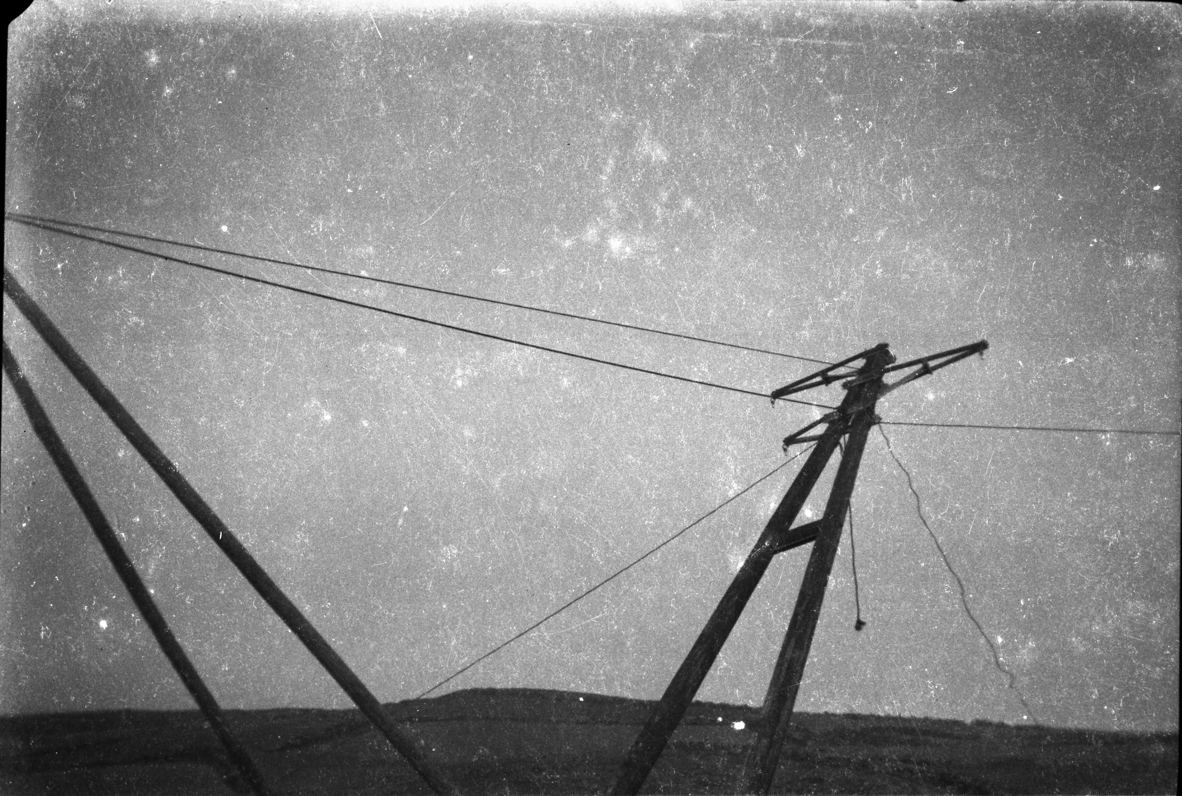 Electricity pole being manoeuvred into position with support wires attached, carrying overhead power lines across a rural landscape.