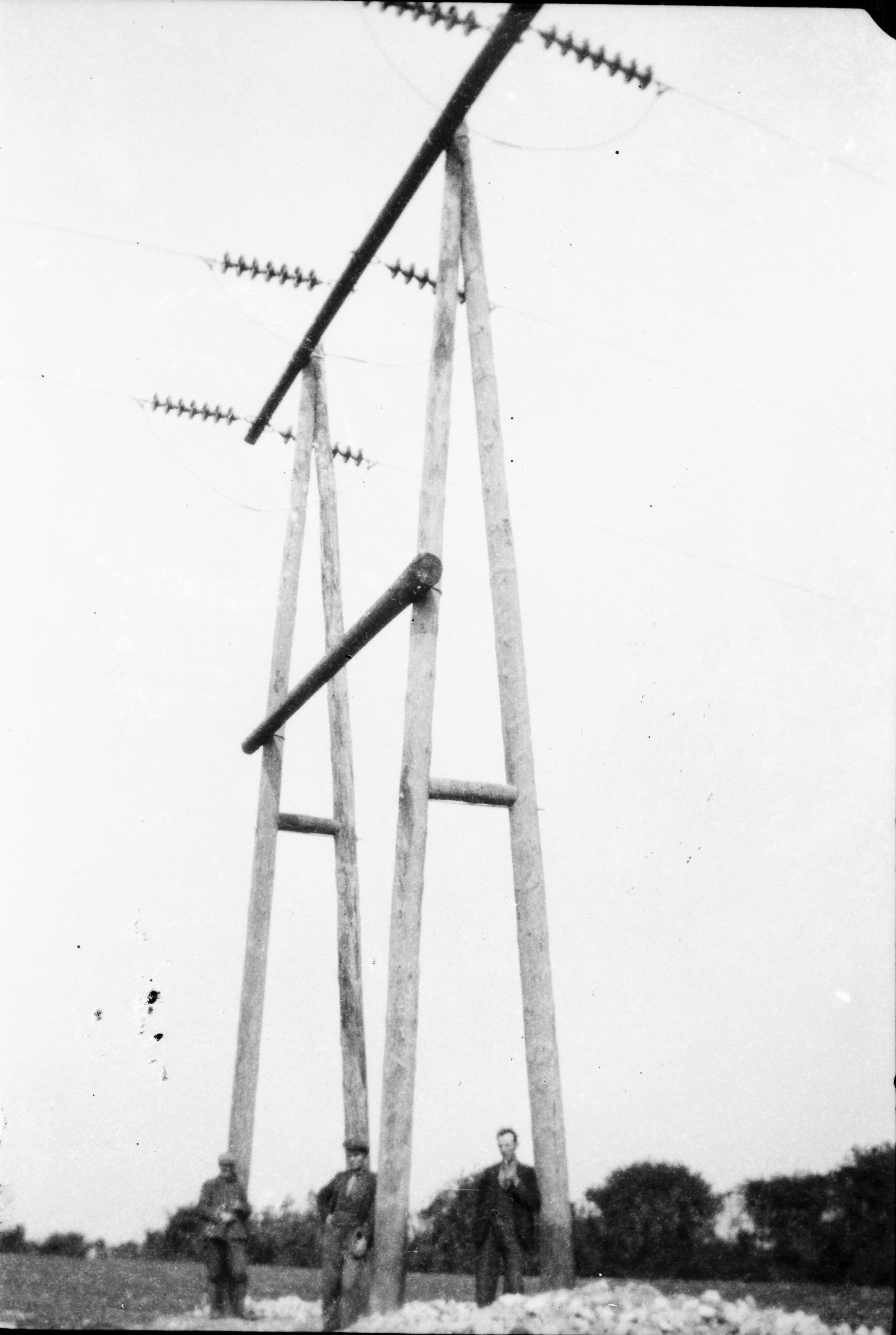 Black-and-white photograph showing a newly erected wooden electricity line structure with insulators and overhead wires, photographed during rural network construction.
