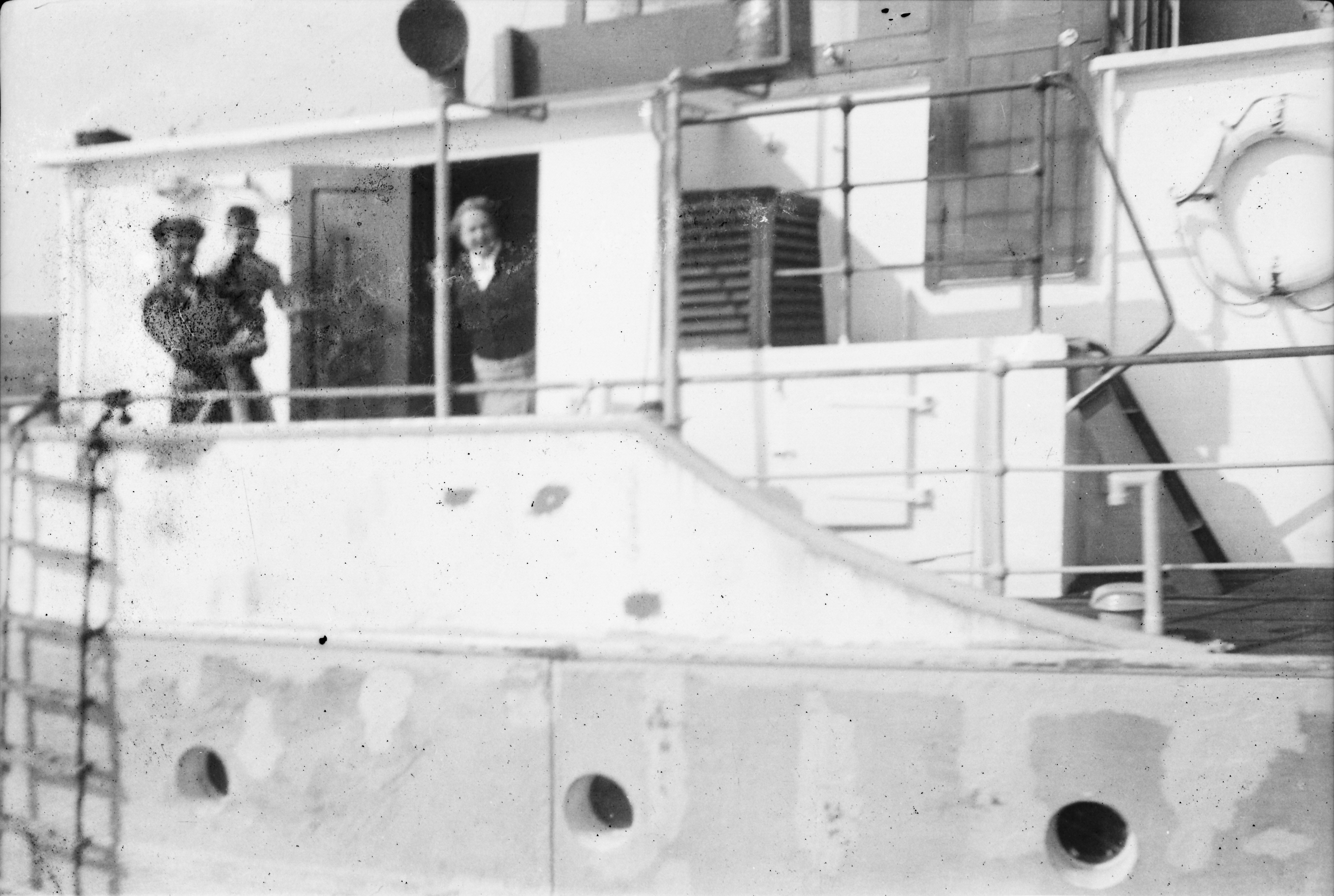 Black-and-white photograph showing Jerry Corbett's wife carrying their son on the deck of a vessel, with railings, lifebuoy housing and cabin structures visible around them.