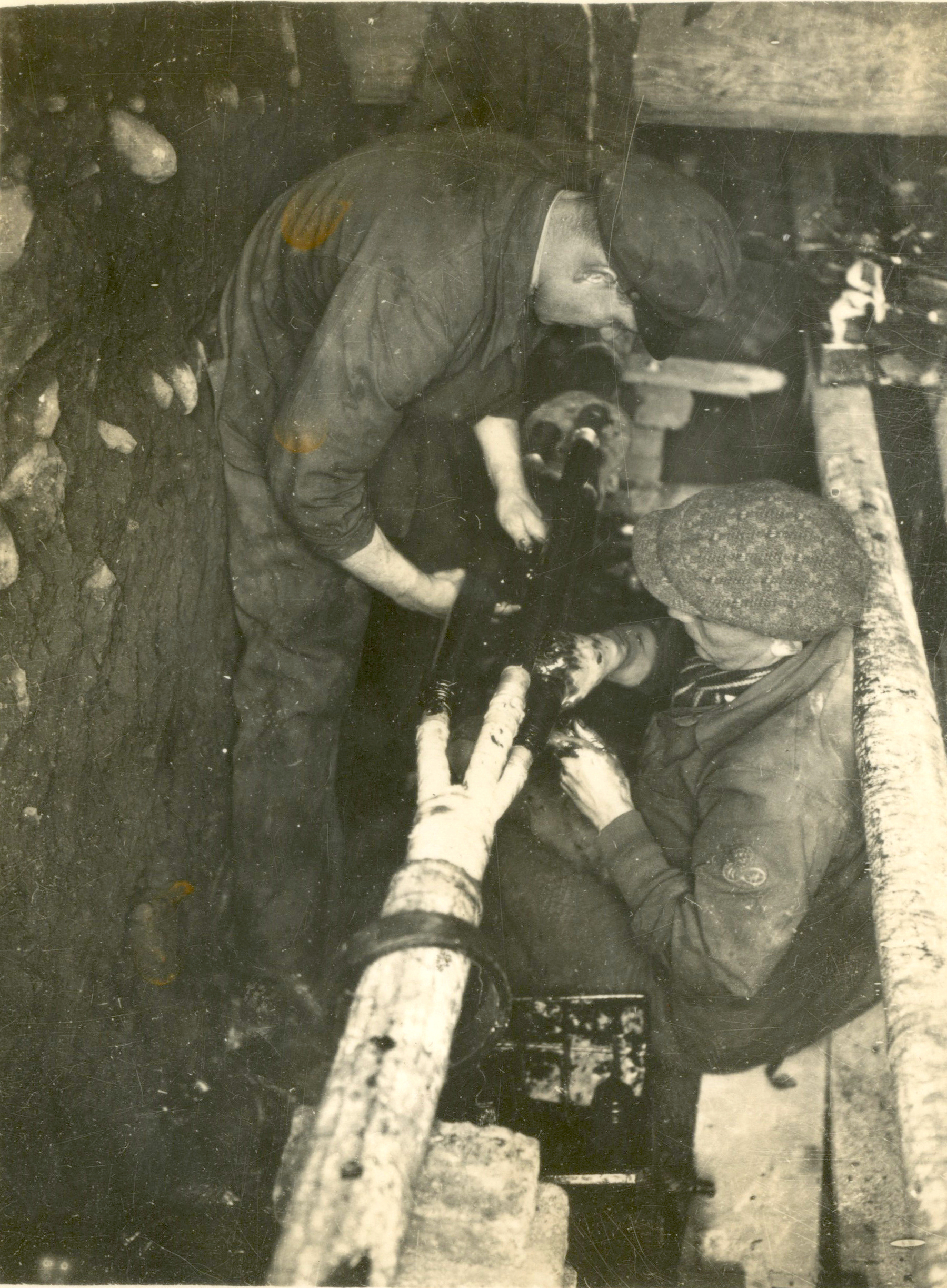 Historic black-and-white photograph showing workers joining and insulating underground electricity cables in a narrow trench during the construction of an electricity distribution network.