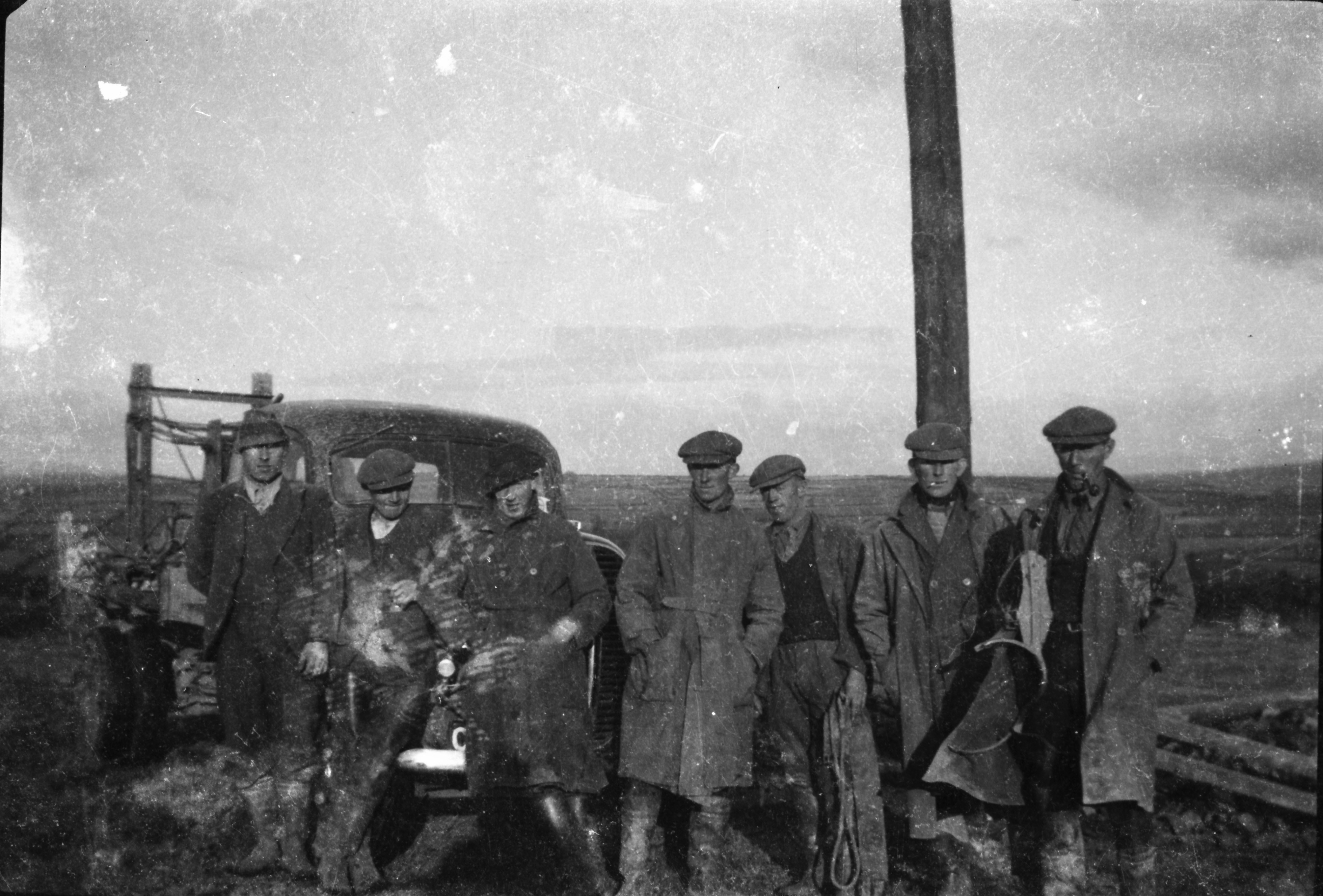 Black-and-white photograph showing a group of workers gathered beside a work truck at an electricity line construction site, with a newly erected wooden pole behind them.
