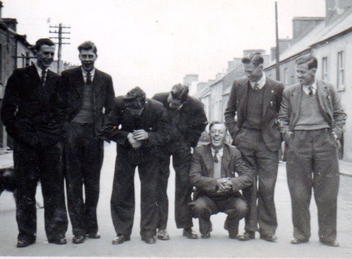 Tim Slevin and colleagues standing together on a village street, posing for a group photograph with rows of houses visible in the background.