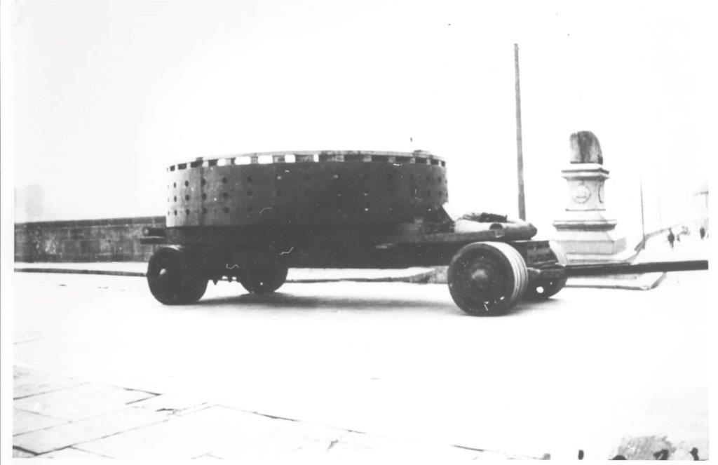 Black-and-white photograph showing a generator component being transported through Limerick city on a multi-wheeled carriage, passing the Treaty Stone on its stone plinth beside the river.