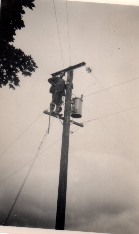 Tim Slevin working from an electricity pole, positioned beside overhead power lines and a transformer mounted on the pole.