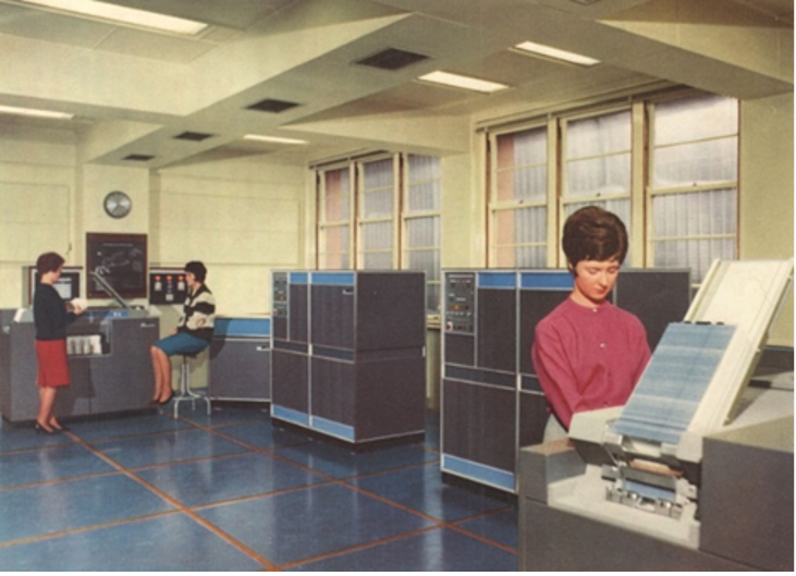 People working in a computer room with large mainframe systems used for data processing.