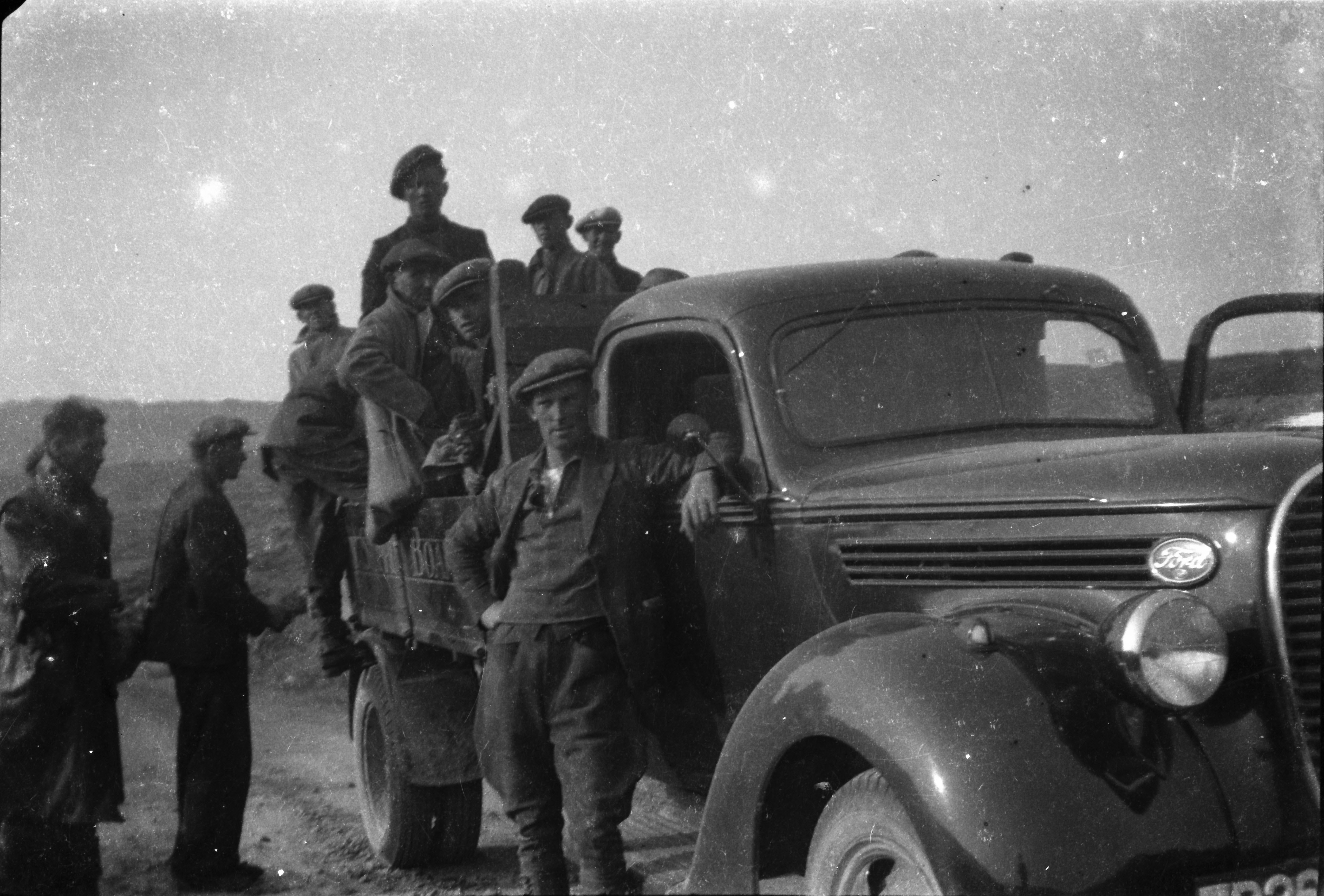 Group of workers gathered around an ESB Ford flatbed truck in a rural landscape, with several people seated in the rear of the vehicle and others standing beside it.