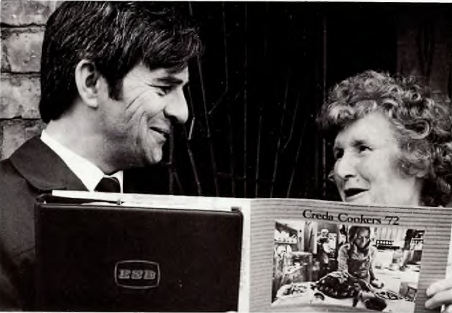 Black-and-white photograph showing an ESB representative discussing electric cookers with a member of the public while holding a promotional brochure about domestic electrical appliances.