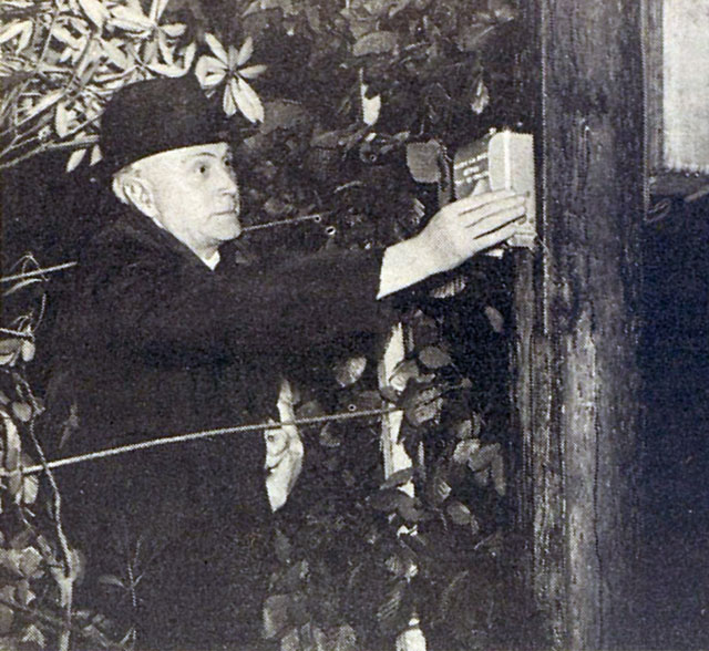Black-and-white photograph showing a person switching on an electrical connection mounted on a wooden pole outdoors.