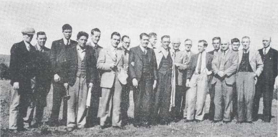 Black-and-white photograph showing a group of people standing together outdoors in an open field.