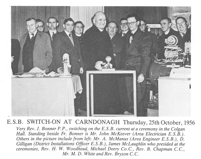 Black-and-white photograph showing a ceremonial switching-on event, with a person operating an electrical switch while a group of attendees gathers around a demonstration display.