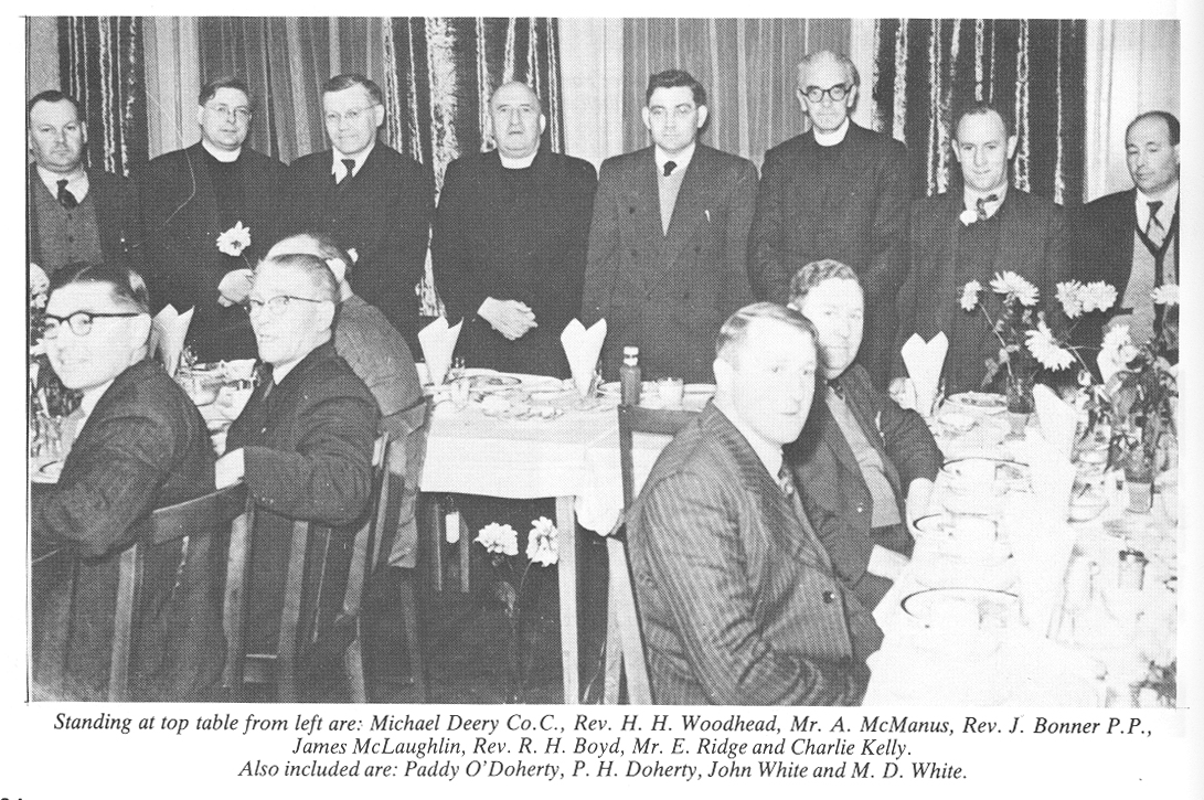 Black-and-white photograph showing attendees seated at a banquet or reception, with a group standing behind the top table.