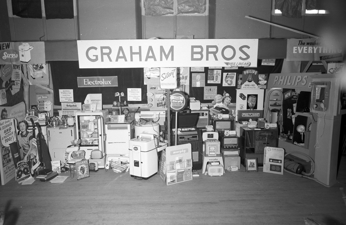 Black-and-white photograph showing an exhibition stand displaying domestic electrical appliances, radios and household equipment at an indoor trade show.