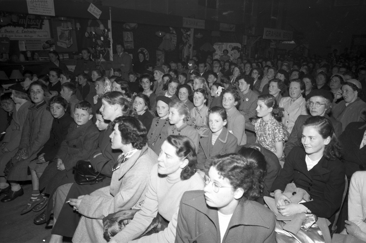 Black-and-white photograph showing a large audience gathered indoors for a public demonstration or community event.