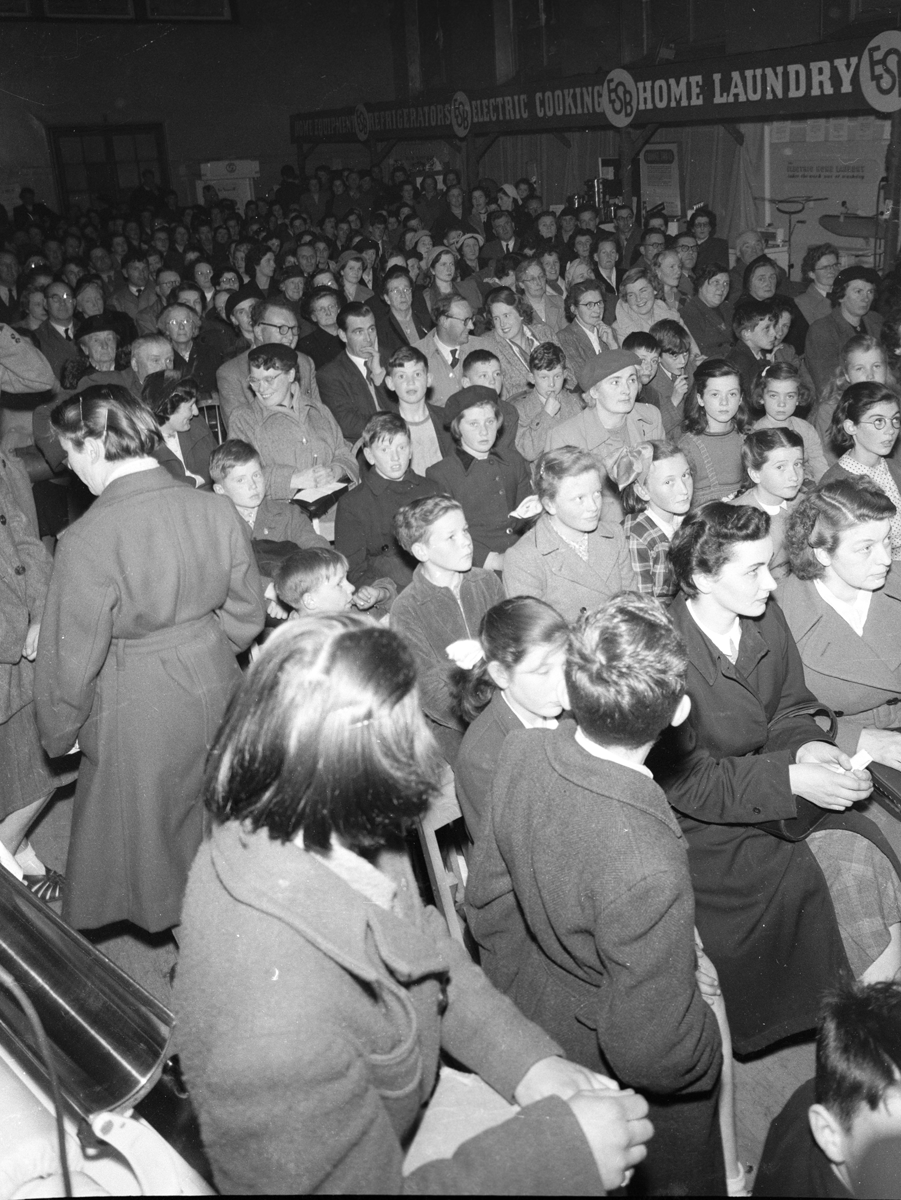 Black-and-white photograph showing a large audience gathered in a hall for an electricity exhibition or community event.