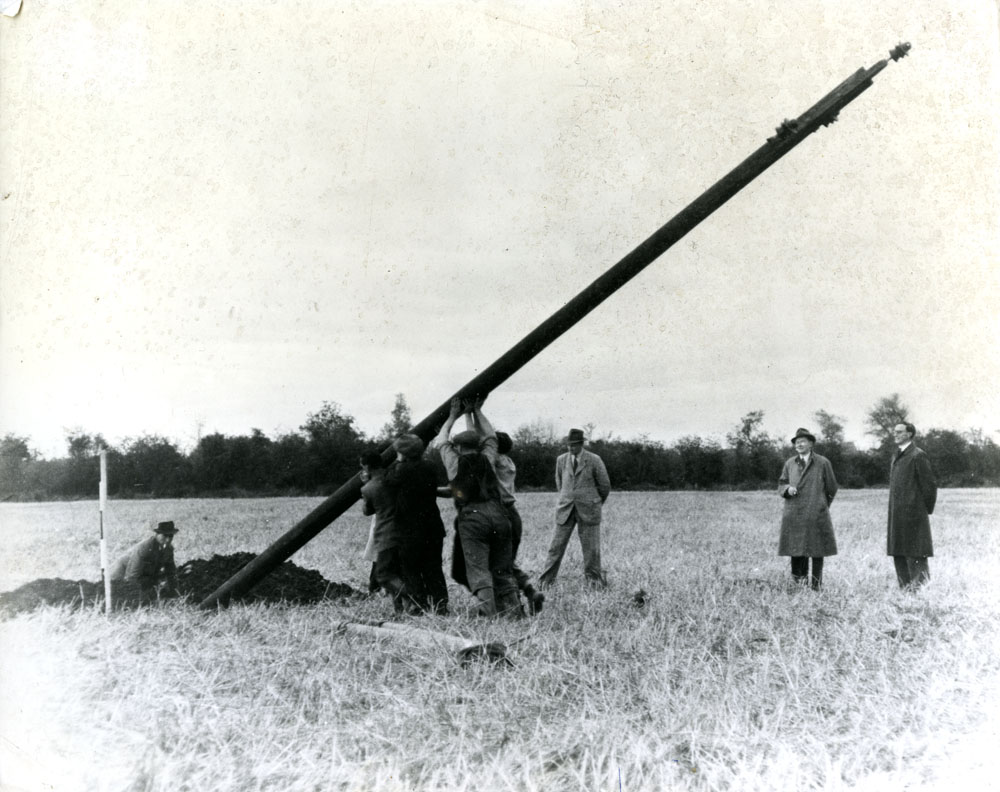 A group of men putting up a pole in a field with onlookers
