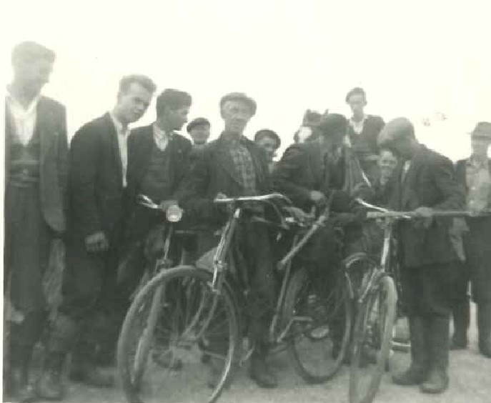 Black-and-white photograph showing a group of rural electrification workers gathered outdoors around two bicycles.
