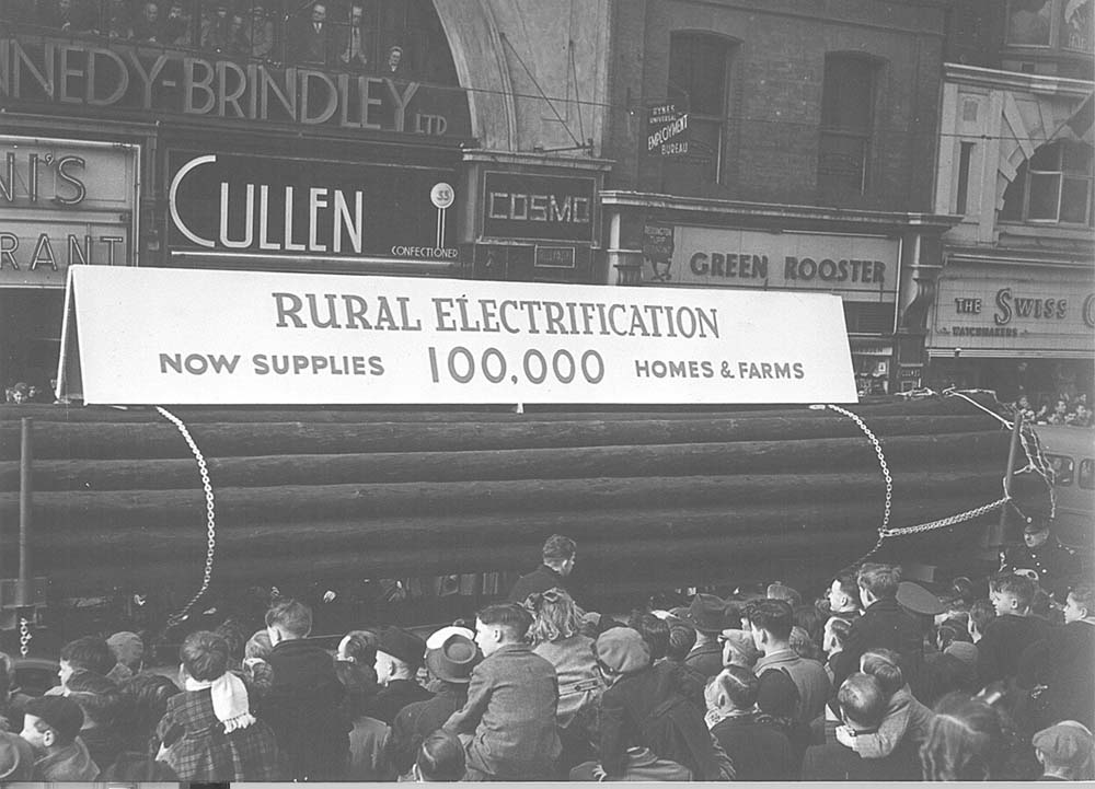 A parade float with a banner 'Rural electrification now supplies 100,000 houses & farms'