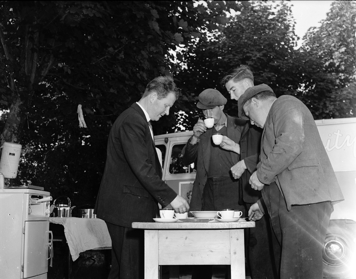 Black-and-white photograph showing several people taking refreshments beside a demonstration area, with electrical cooking equipment and an ESB promotional vehicle visible nearby.