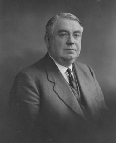 Portrait photograph of Dr Thomas McLaughlin seated in a suit and tie.