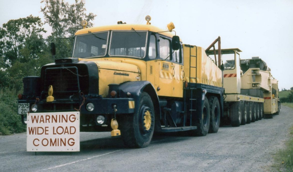 Colour photograph showing an ESB heavy haulage vehicle towing a multi-axle trailer during the transport of oversized electrical equipment along a rural road.